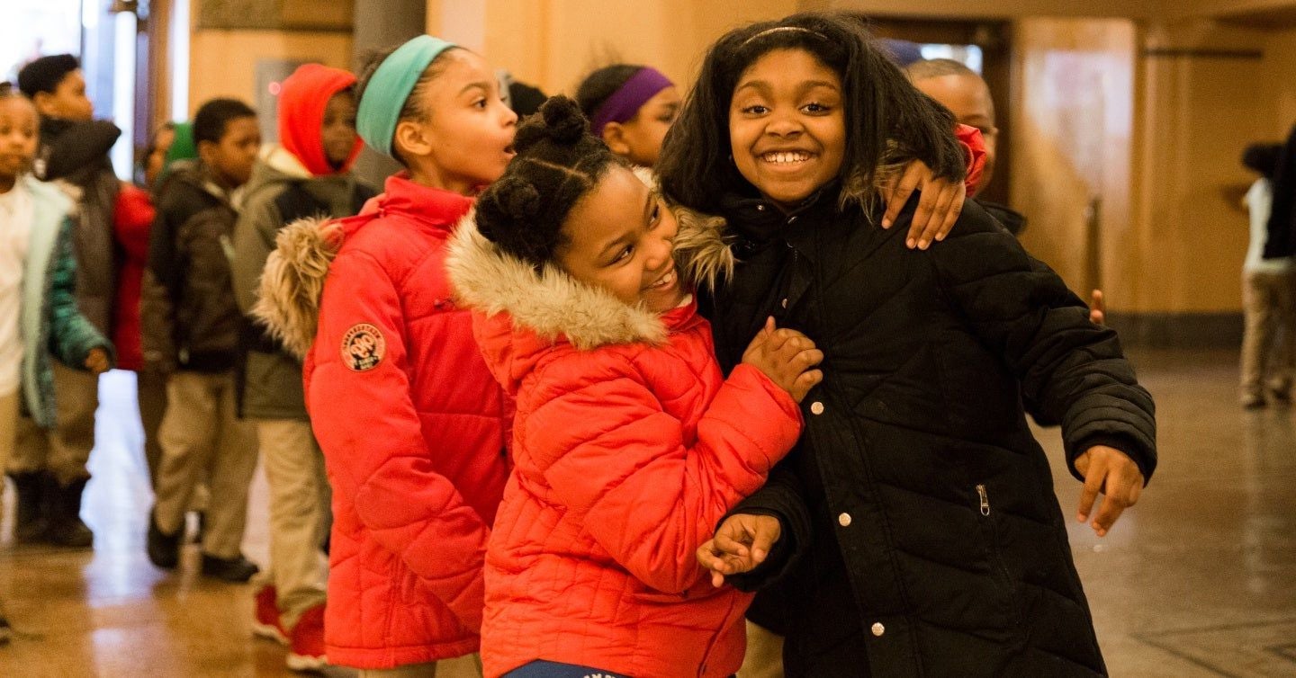 A group of happy children hugging each other tightly in the theatre lobby.