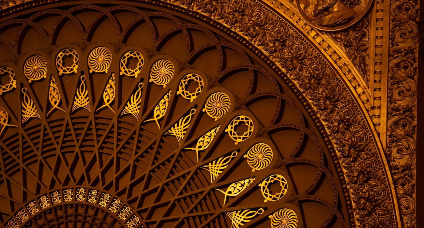 Ornate circular ceiling design features intricate gold patterns with spirals and floral motifs on a warmly lit background.